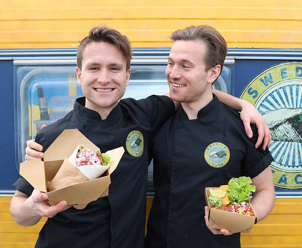 Foodtruck med ägarna framför som håller maten